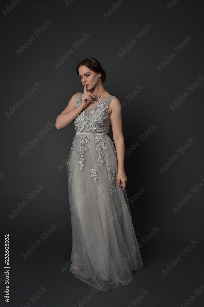 full length portrait of brunette girl wearing long silver ball gown. standing pose on grey studio background. full length portrait of brunette girl wearing long silver ball gown. standing pose on grey studio background.