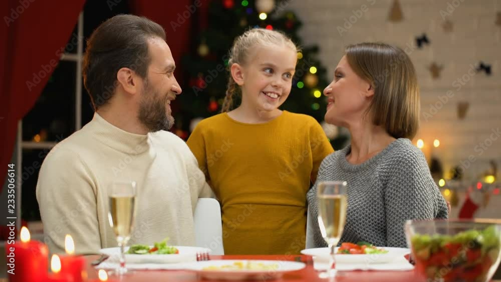 Happy parents kissing adorable daughter on Xmas eve, family celebrating holiday Happy parents kissing adorable daughter on Xmas eve, family celebrating holiday