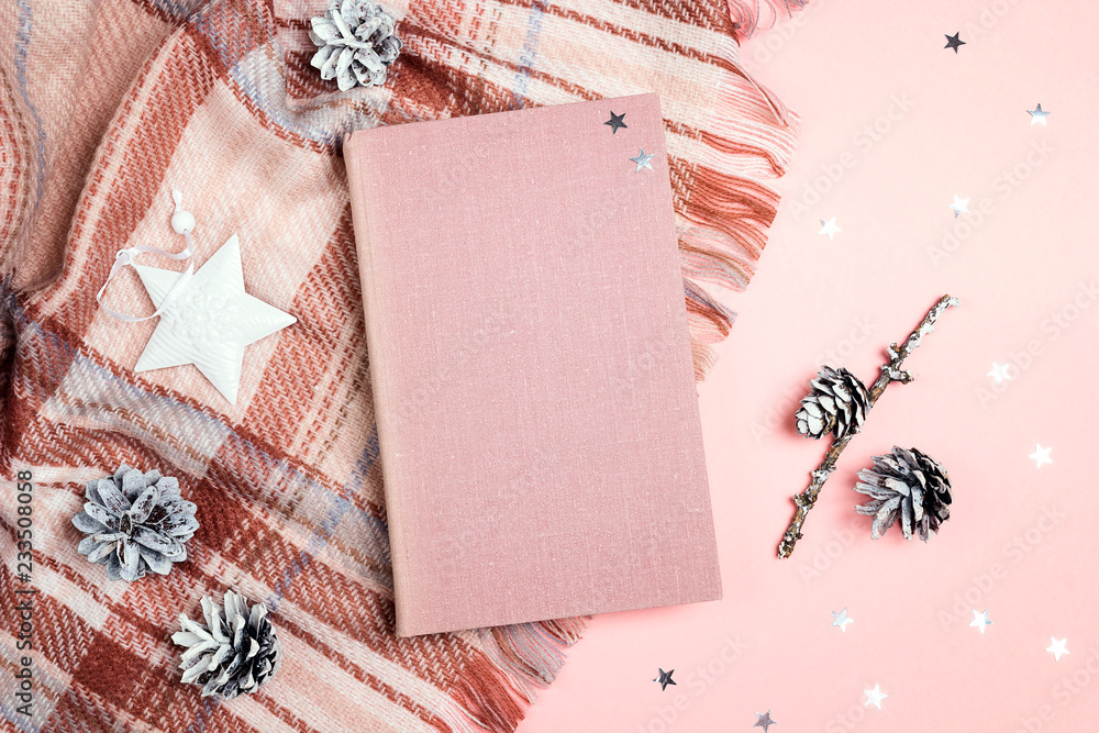 Naklejka premium Top-down winter holidays composition with book, plaid, cones and stars on pink background.