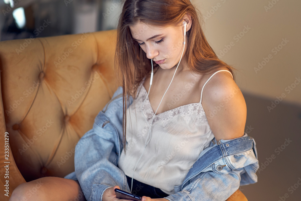 Fototapeta premium Relax in the rhythm of my music. Attractive young woman lwith earphones and smartphone sitting on sofa at home.