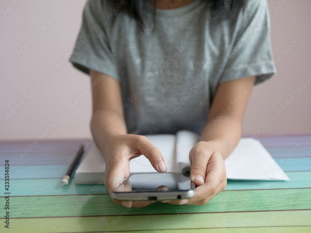 Fototapeta premium A little girl playing smartphone with doing homework