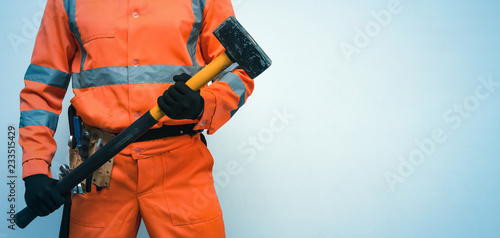 Builder worker holding in hands a big sledgehammer isolated on blue background with copy space. Under construction concept.