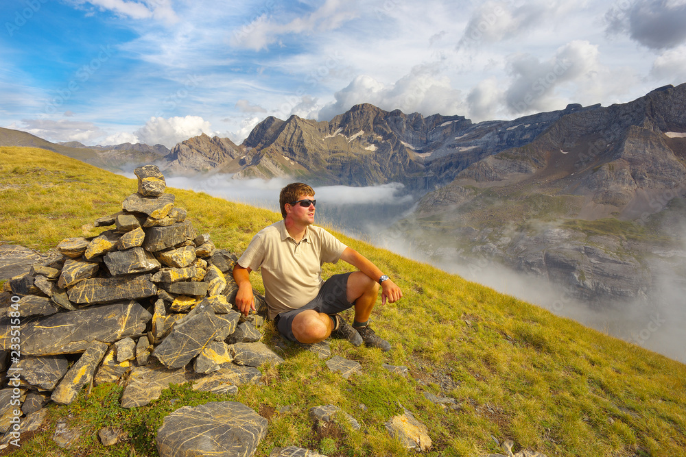Resting tourist on the ridge next to the stone pile with mountains on backround, Pyrenees