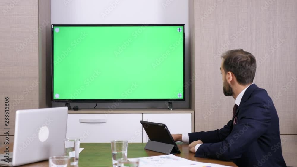 Businessman in conference video call via a big green screen TV. Dolly slider 4K footage Businessman in conference video call via a big green screen TV. Dolly slider 4K footage