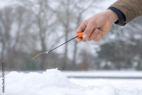 Winter fishing concept. Hand of fisherman with specialised rod above snowy ice.
