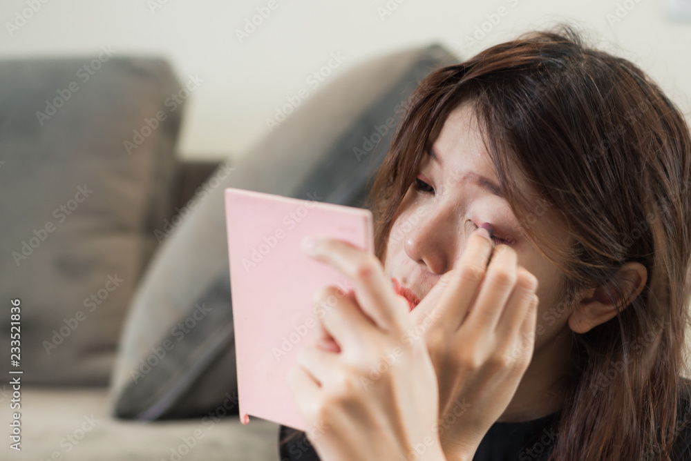 Asian young woman looks into pink pocket mirror and putting eye pencil color on eyes. Makeup beauty care woman. Asian young woman looks into pink pocket mirror and putting eye pencil color on eyes. Makeup beauty care woman.