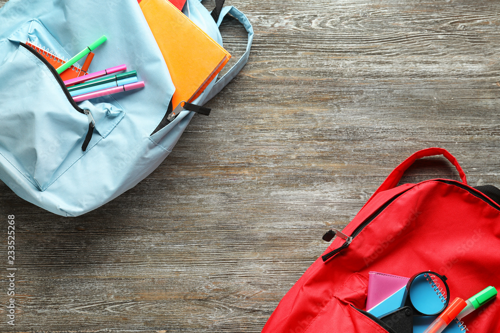 Naklejka premium Color rucksacks with school stationery on wooden background