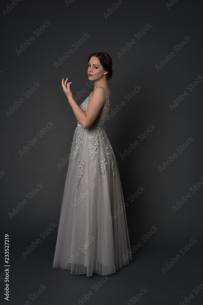 full length portrait of brunette girl wearing long silver ball gown. standing pose on grey studio background. full length portrait of brunette girl wearing long silver ball gown. standing pose on grey studio background.