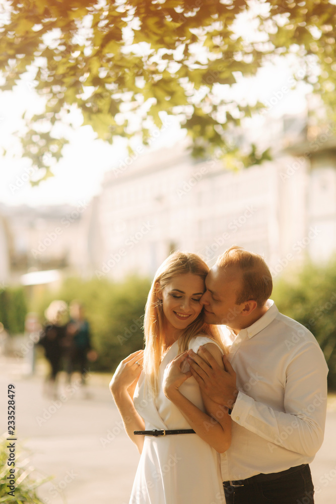 Fototapeta premium Young beautiful couple husband in a white shirt and a woman in a dress walking around the park in summer time