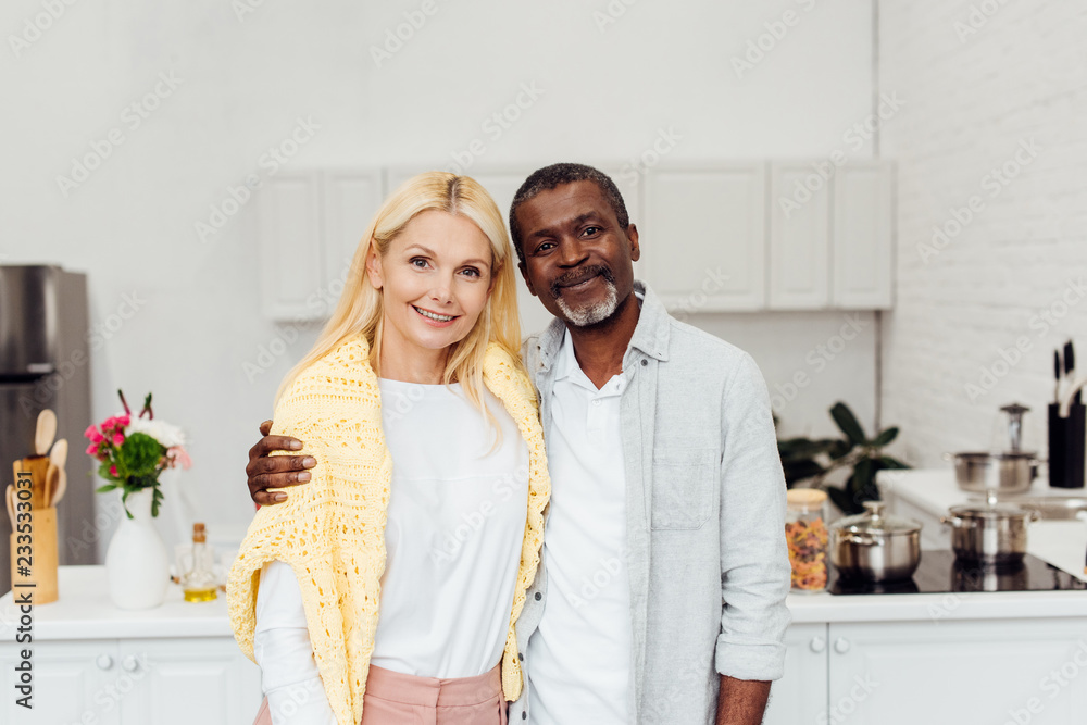african american man hugging blonde mature woman at kitchen african american man hugging blonde mature woman at kitchen