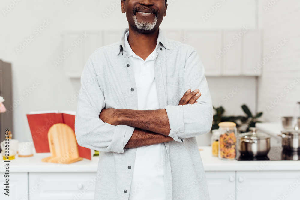 cropped view of african american man with arms crossed standing at kitchen cropped view of african american man with arms crossed standing at kitchen