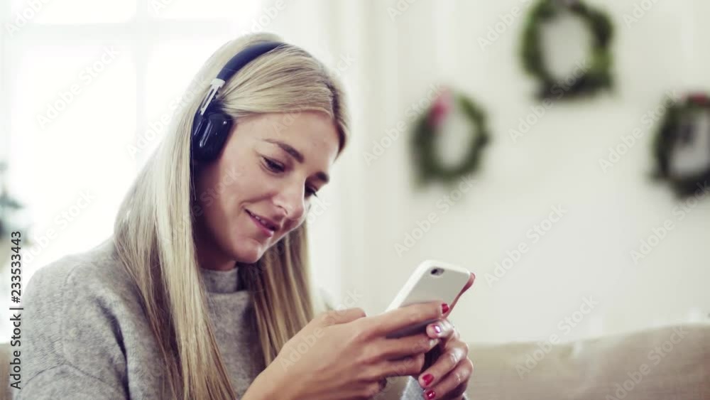 A young woman with headphones and smartphone at home at Christmas time. A young woman with headphones and smartphone at home at Christmas time.