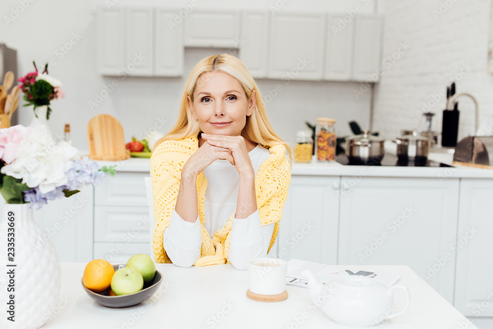 smiling woman sitting at kitchen and drinking tea in morning smiling woman sitting at kitchen and drinking tea in morning