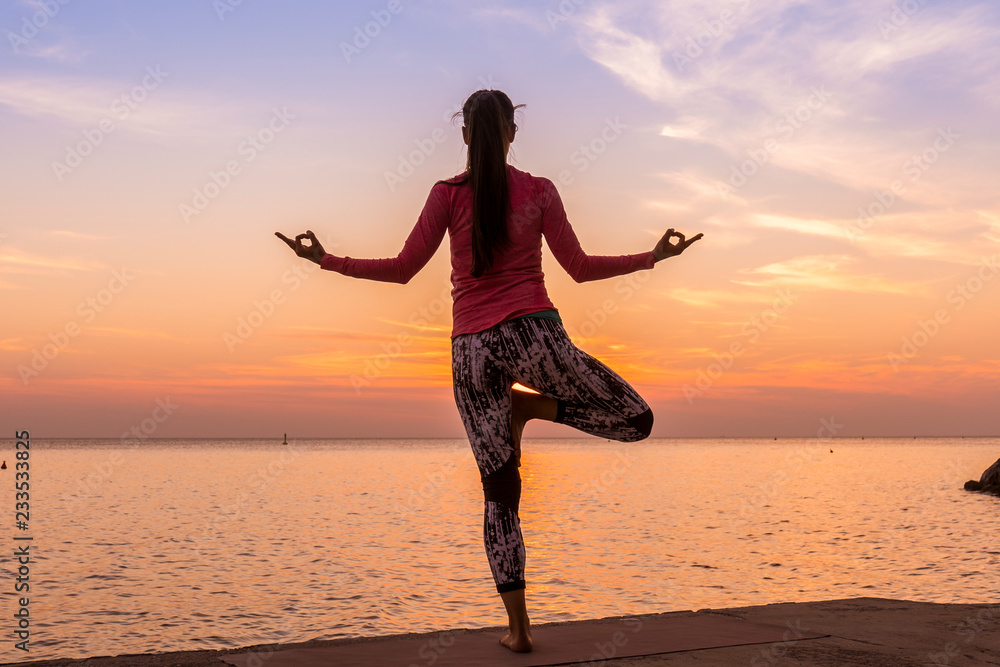 Young beautiful woman practicing Yoga by the sea at sunset