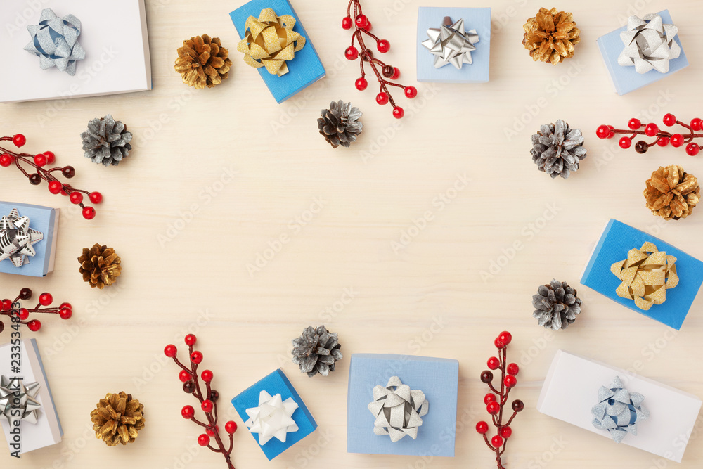 Fototapeta premium Christmas composition of fir cones, gift boxes and red berries, laid out in a circle. Copy space on a light wooden background.