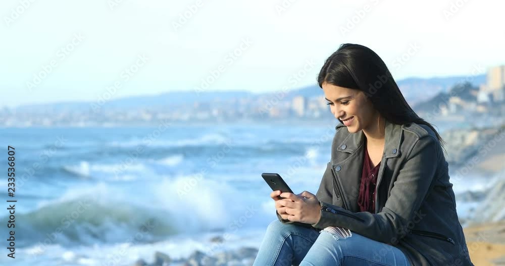Happy teenage girl texting on smart phone sitting on the beach Happy teenage girl texting on smart phone sitting on the beach