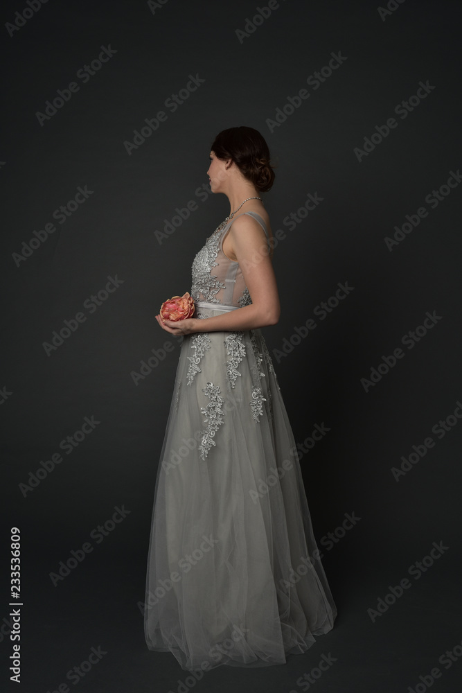 Naklejka premium full length portrait of brunette girl wearing long silver ball gown. standing pose on grey studio background.