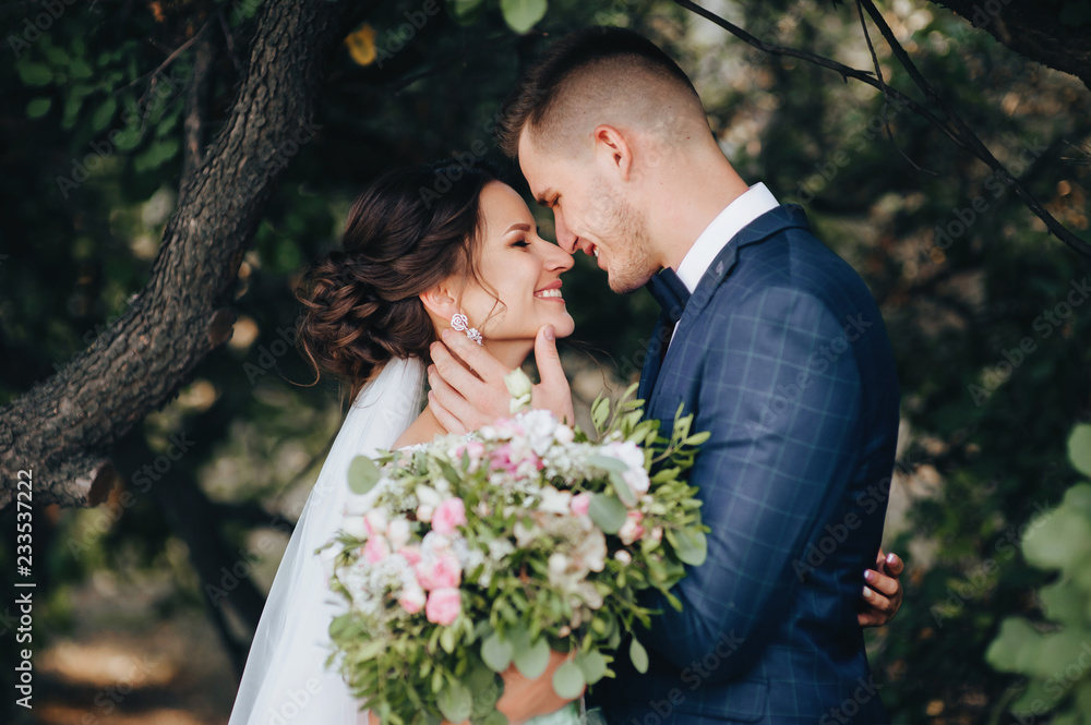 Beautiful newlyweds hugging and smiling in a green garden with trees. Young bride and cute bride close-up. Wedding photography. Stylish portrait. Beautiful newlyweds hugging and smiling in a green garden with trees. Young bride and cute bride close-up. Wedding photography. Stylish portrait.