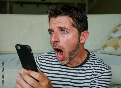 young perplexed and shocked man using mobile phone looking internet social media or checking news in surprised and crazy disbelief face expression feeling petrified