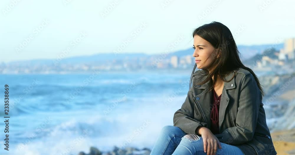 Relaxed teenage girl looking at horizon on the beach with the sea in the background Relaxed teenage girl looking at horizon on the beach with the sea in the background