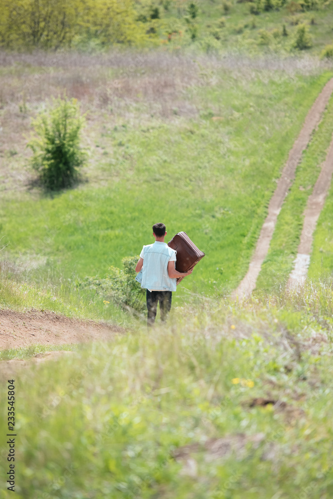 Teenager with suitcase in hands walking on old road Teenager with suitcase in hands walking on old road