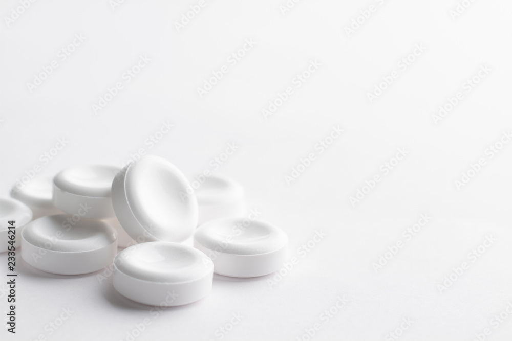 A handful of large white tablets lies on a white background. Concept on the topic of medicines with space for text. Excellent light minimalistic background in high key.