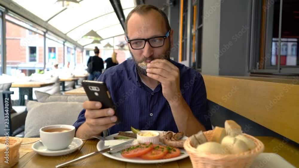 Man texting on smartphone and eating breakfast in cafe Man texting on smartphone and eating breakfast in cafe