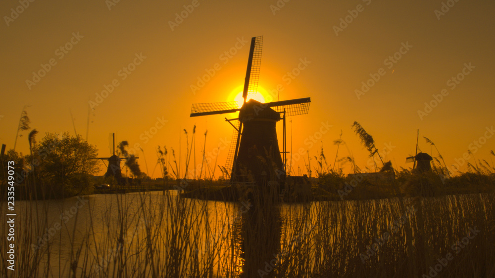 Stunning authentic old windmill on the river bank at beautiful golden evening