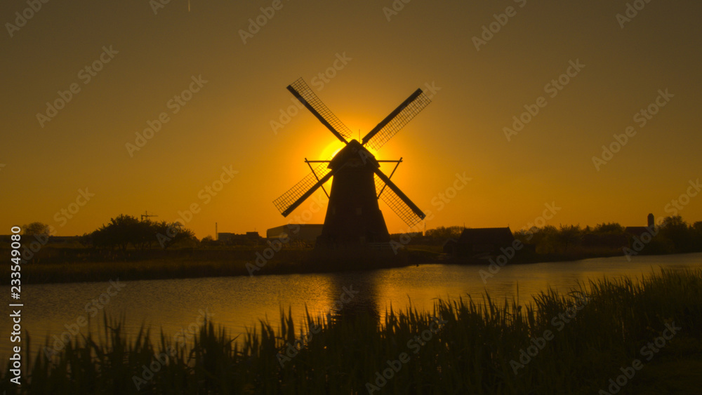 Beautiful authentic old windmill on the river bank at beautiful golden dawn