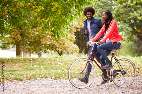 Black man running in a park beside his girlfriend, who is riding a bike, side view