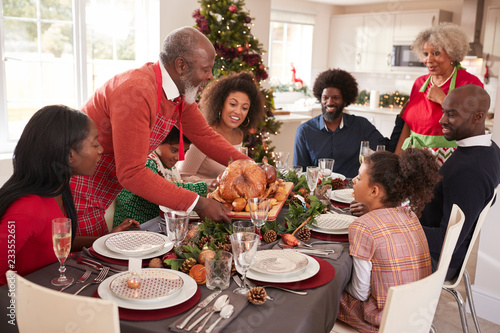 Grandfather bringing the roast turkey to the dinner table during a multi generation  mixed race family Christmas celebration  elevated view