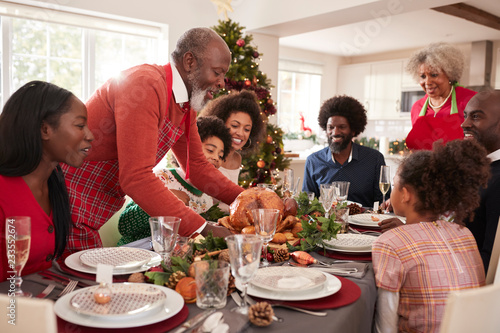 Grandfather bringing the roast turkey to the dinner table during a multi generation  mixed race family Christmas celebration  close up