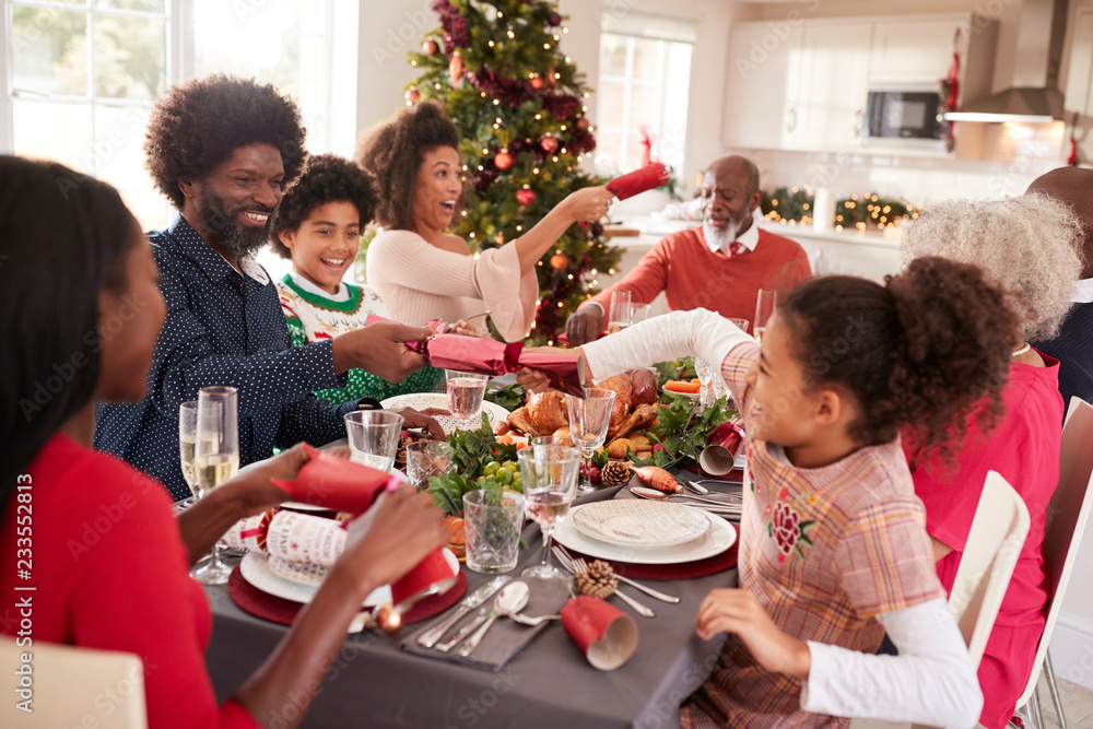 Mixed race, multi generation family having fun pulling crackers at the Christmas dinner table Mixed race, multi generation family having fun pulling crackers at the Christmas dinner table