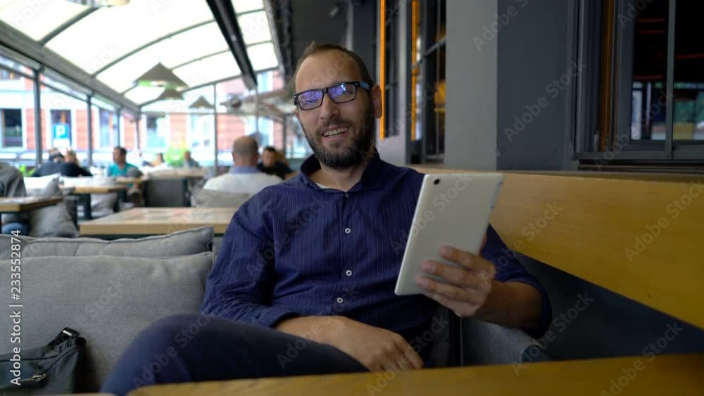 Young man with tablet talking to camera at cafe Young man with tablet talking to camera at cafe