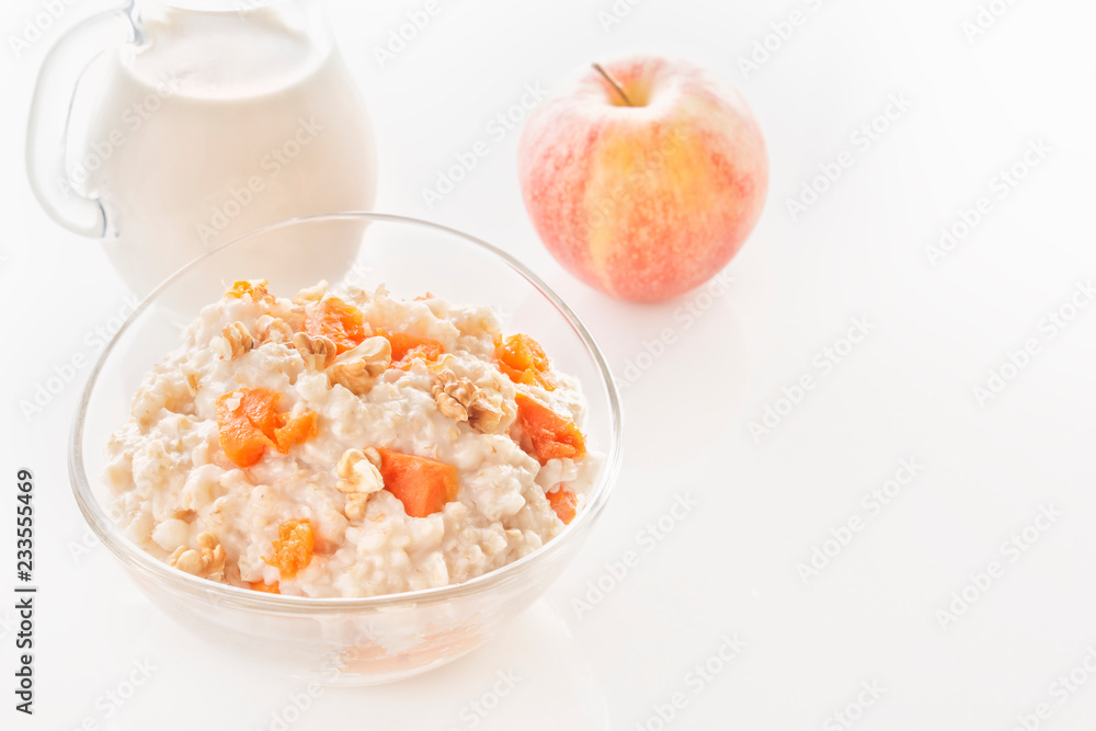 Oatmeal with pumpkin and nuts in a glass plate and a jug with milk on a white background. Close-up. Copy space Oatmeal with pumpkin and nuts in a glass plate and a jug with milk on a white background. Close-up. Copy space