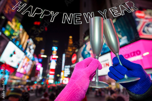 Winter gloved hands doing a holiday toast under shiny Happy New Year bunting in front of the crowds and bright lights of Times Square, New York City