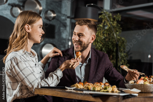 Beautiful smiling young woman feeding her boyfriend with sushi in restaurant