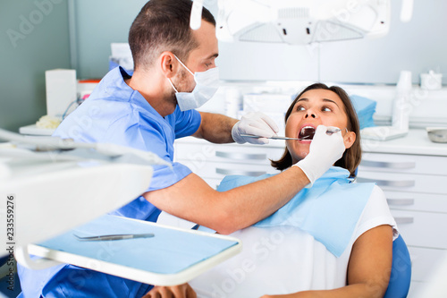 Dentist is treating woman patient which is sitting in dental chair