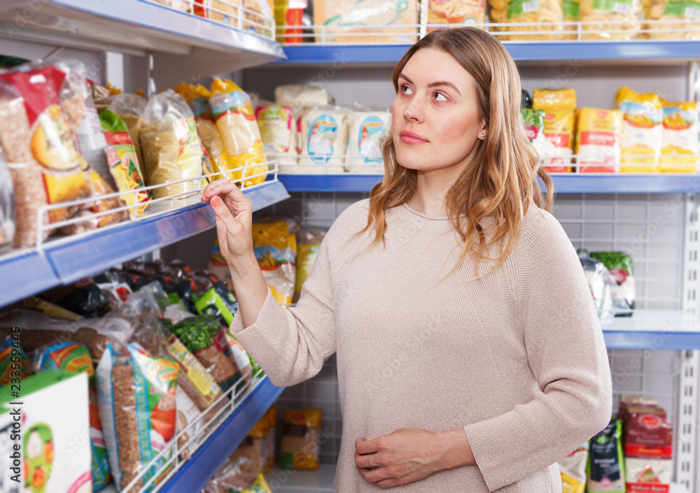 Positive woman buyer choosing groats in  grocery food store