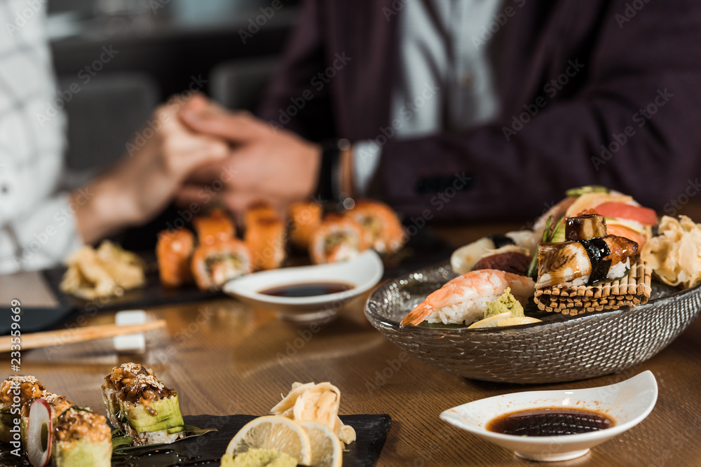 Fototapeta premium Sushi rolls and seafood on the background of couple holding hands