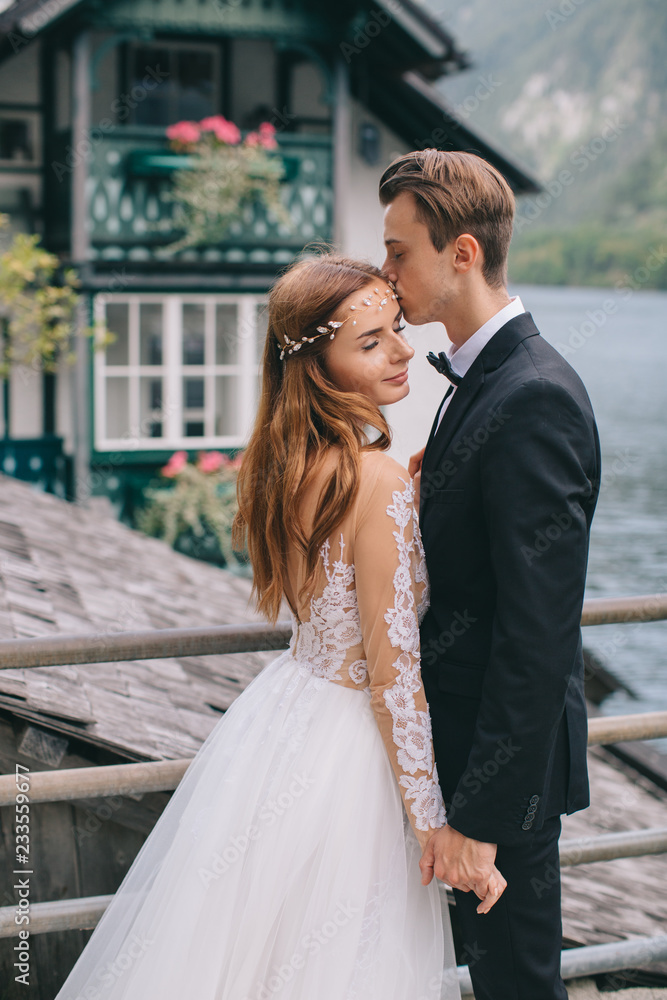 A beautiful wedding couple walks on the lake and mountains background in a fairy Austrian town, Hallstatt.