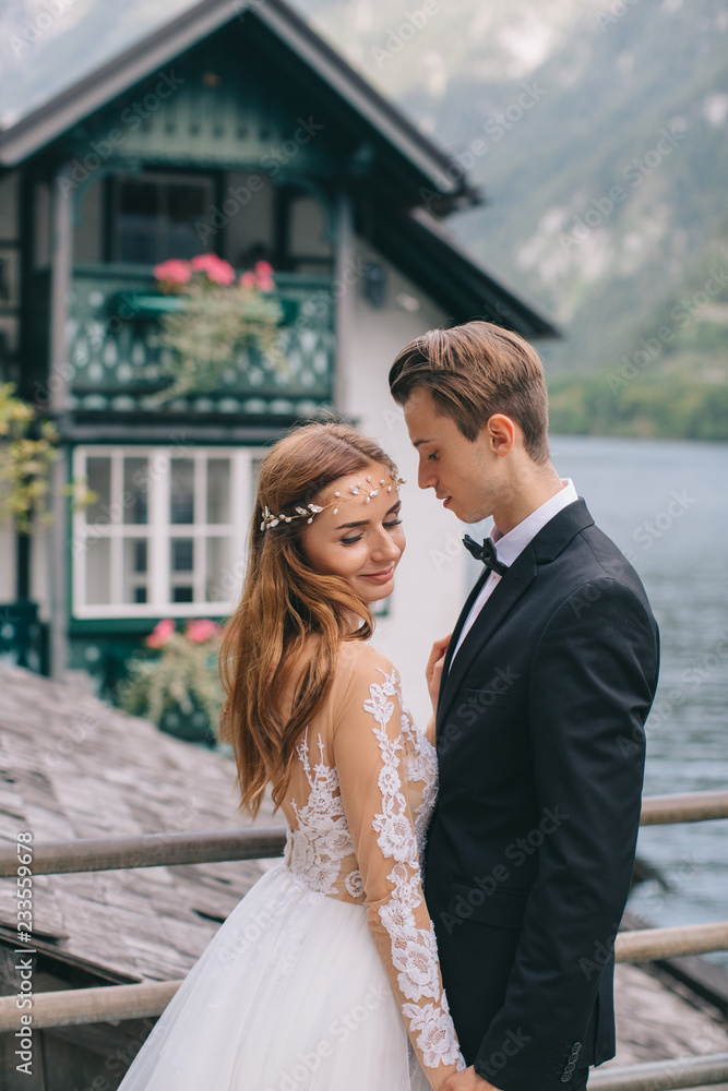 Naklejka premium A beautiful wedding couple walks on the lake and mountains background in a fairy Austrian town, Hallstatt.