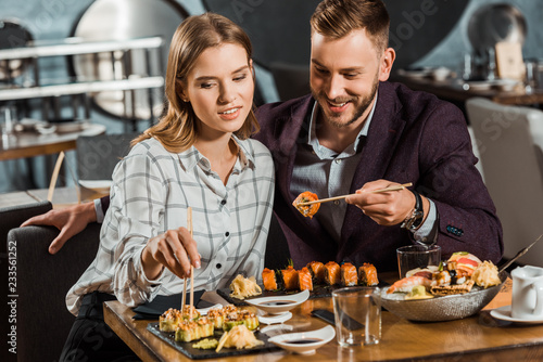 Happy smiling young adult couple eating sushi rolls in restaurant