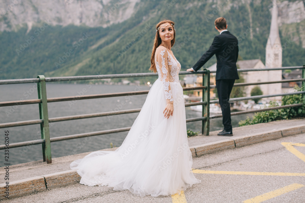 A beautiful wedding couple walks on a background old cathedral, lake and mountains in a fairy Austrian town, Hallstatt. A beautiful wedding couple walks on a background old cathedral, lake and mountains in a fairy Austrian town, Hallstatt.