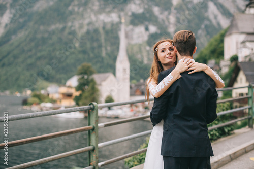 A beautiful wedding couple walks on a background old cathedral, lake and mountains in a fairy Austrian town, Hallstatt.