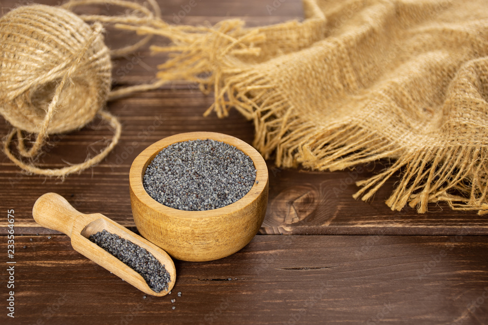 Composition of lot of whole czech blue poppy seeds with wooden bowl on brown wood Composition of lot of whole czech blue poppy seeds with wooden bowl on brown wood