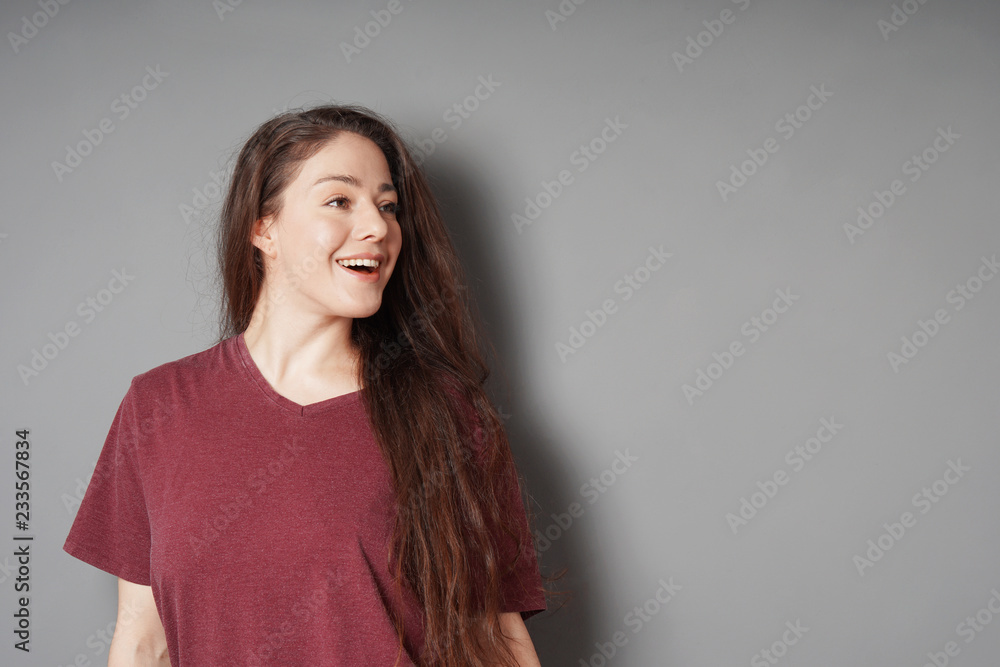 happy smiling young woman in her 20s with natural make-up and brunette long hair looking to side with copy space on gray background happy smiling young woman in her 20s with natural make-up and brunette long hair looking to side with copy space on gray background