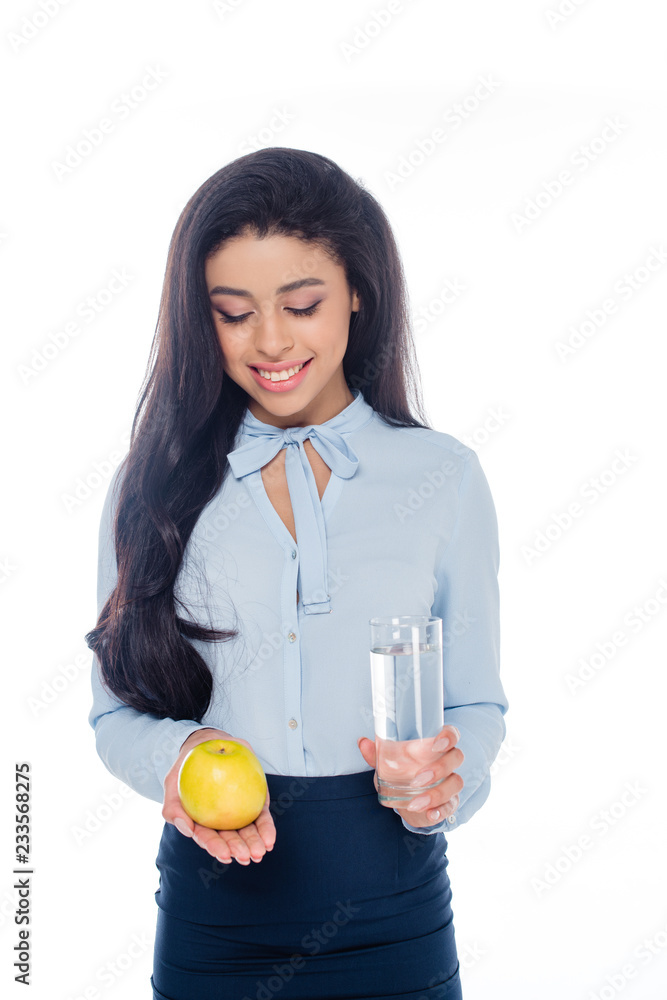 smiling young african american woman holding glass of water and apple isolated on white smiling young african american woman holding glass of water and apple isolated on white