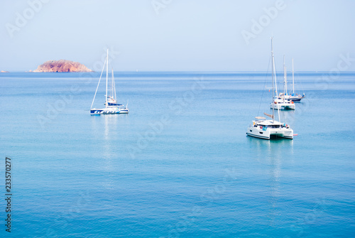 Two catamarans and three sailboats anchored in the middle of the sea
