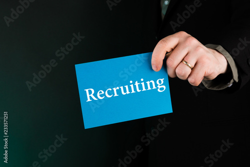 Businessman holding blue card with text "Recruiting", man in suit,gradient blue background, Concept job recruitment and human resource